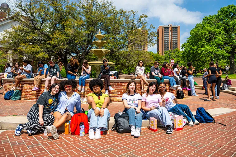 A large group of TWU students on the Denton campus relax around the fountain at an event.