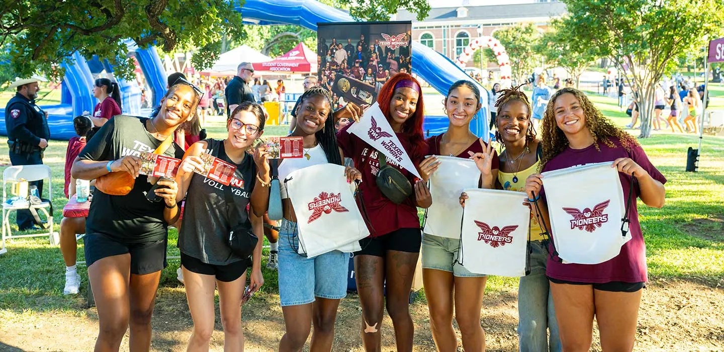 A group of TWU students take a photo and holding Pioneers athletics themed items.