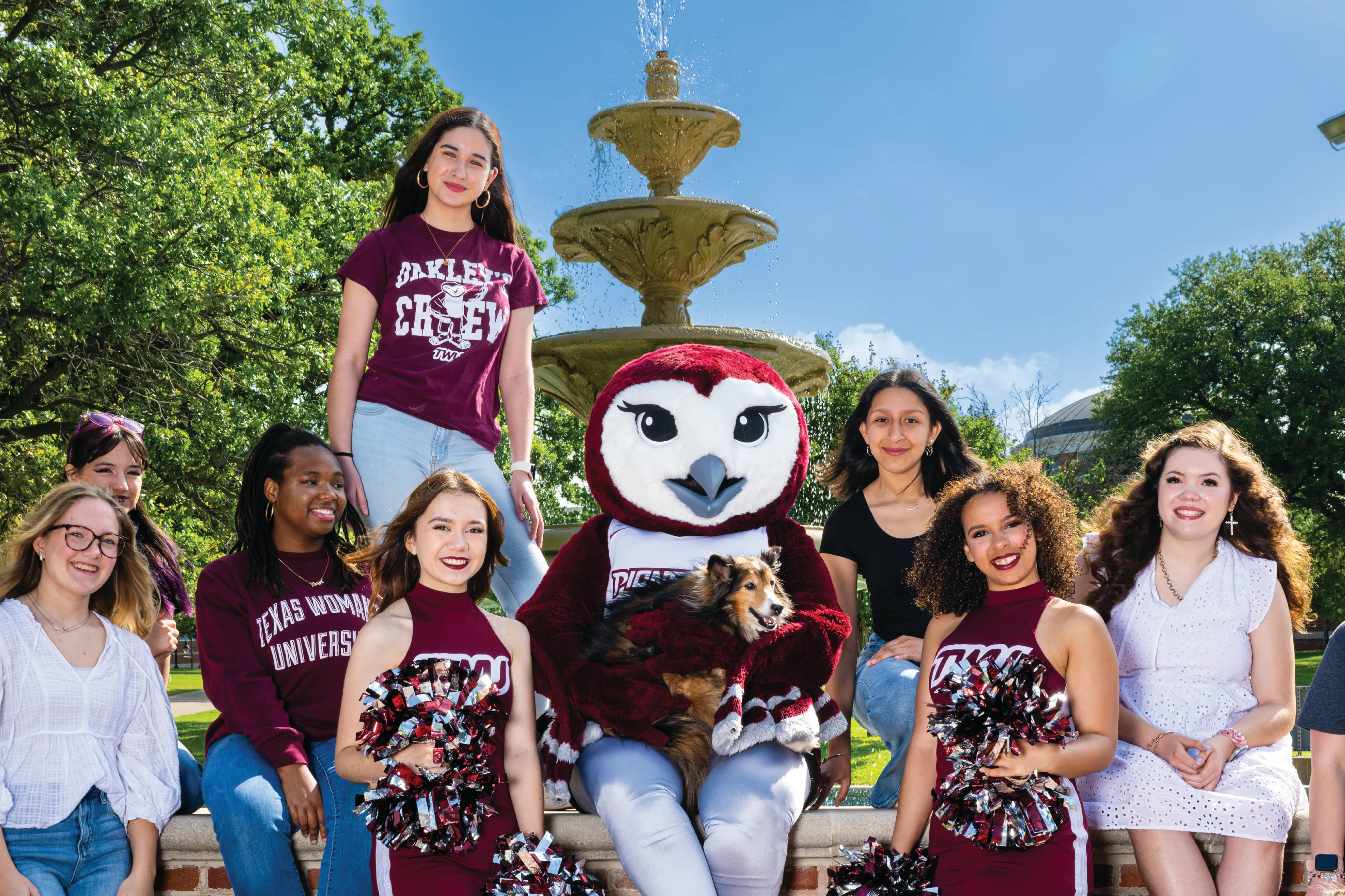 A group of TWU students stand around the Denton campus fountain for a group photo with Oakley.