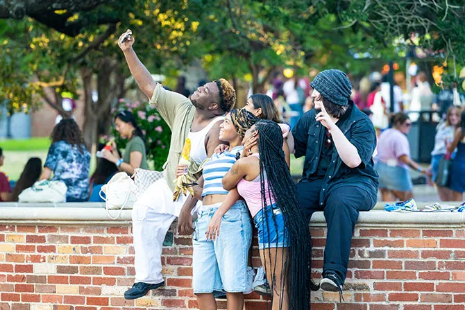 A group of TWU students stand around the Denton campus fountain and take a selfie.