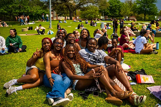 A group of TWU students sit together on the lawn in front of Hubbard Hall at an event.
