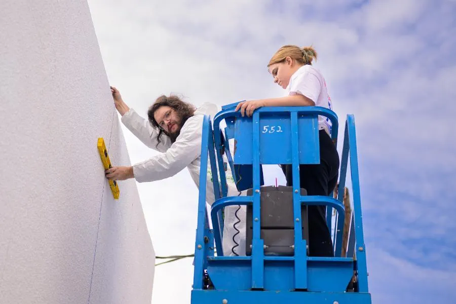 Students on scissor lift work on campus mural 