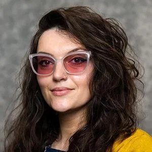 Portrait of Kristina Smith. Long wavy hair, wearing rose-tinted glasses
