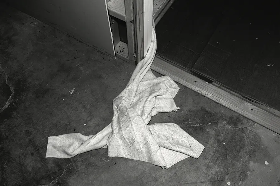 black and white image, womans sweater lay in a ball in doorway, on top of floor stain