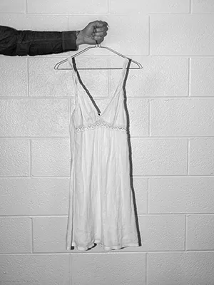 black and white image, an arm (body out of frame), holds up a womens slip hanging from a wire hanger