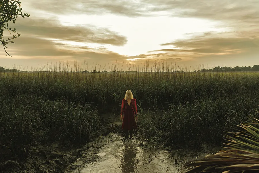 A blonde women stands in a marsh, with golden light from the setting sun