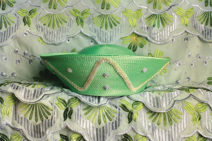 a light green wide brim hat is folded to look like a paper ship, sitting atop a light green patterned background