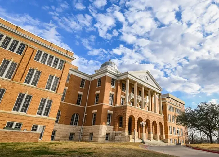 Image of front entrance to the Old Main Building, brownish red brick building with white columns