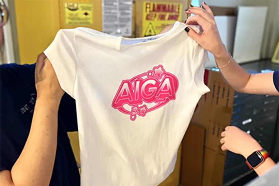 Two students hold up a T-shirt they silkscreened with the Aiga TWU logo, during a screen printing workshop