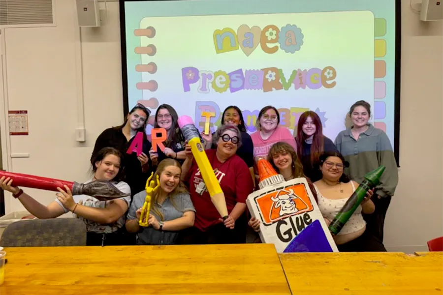 Laura Lee poses with the NAEA Preservice Pioneers, an Art Education Student Organization, during their first meeting, holding oversized paper mâché school art supplies - 900x600