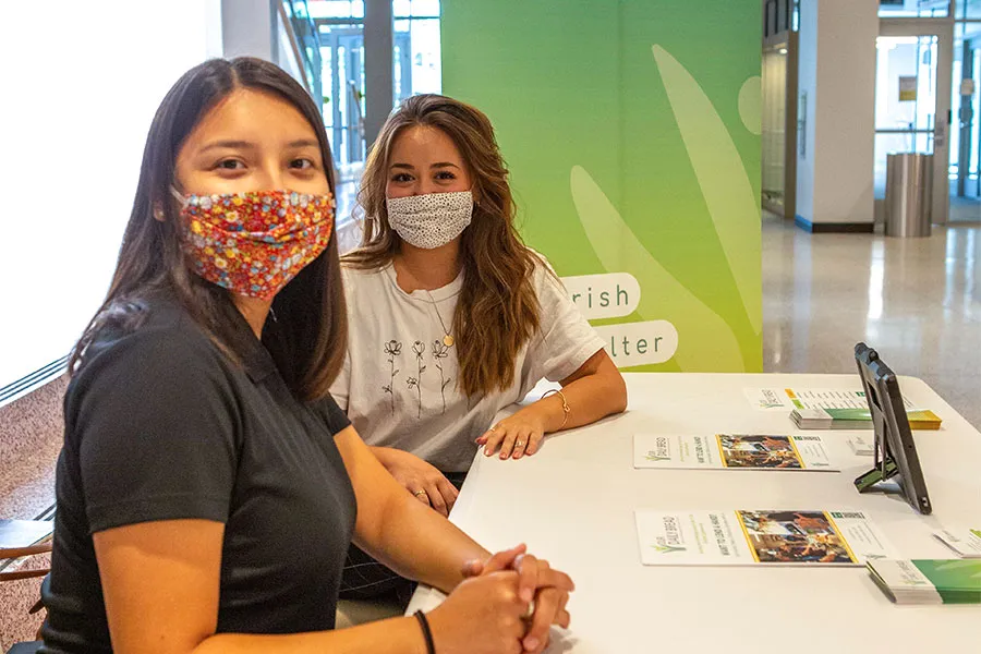 Two young women in protective face masks work a fair table