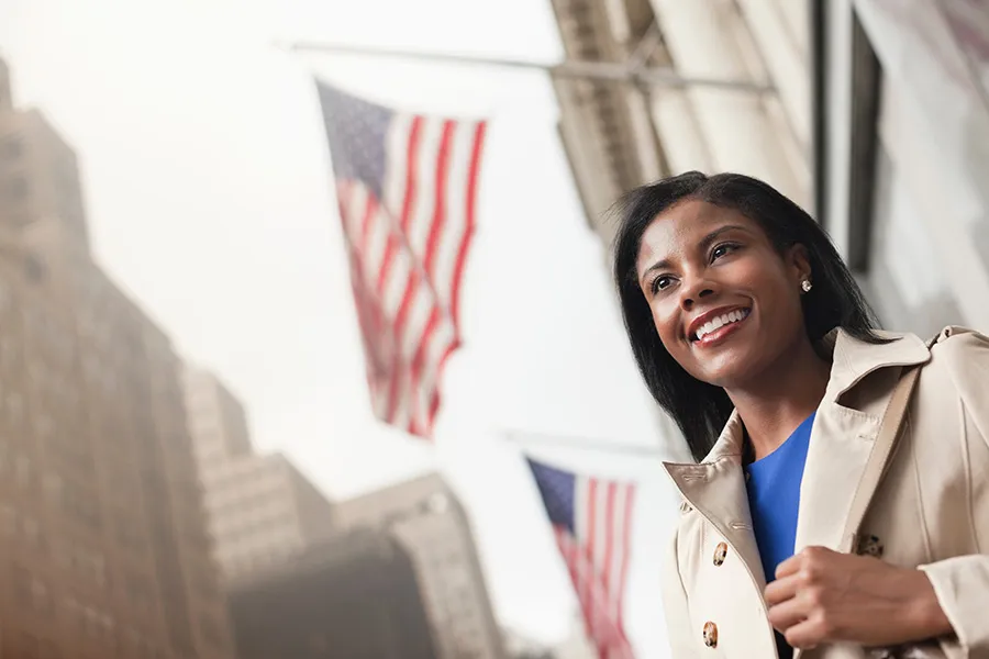 A woman stands on a city street with American flags waving above her