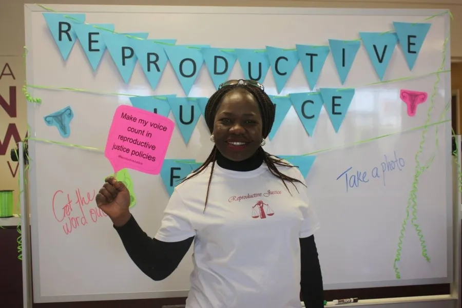 Esther Ajayi-Lowo, MWGS doctoral candidate and planning committee chair, shows off one of the message signs for the photo booth at the reproductive justice fair.