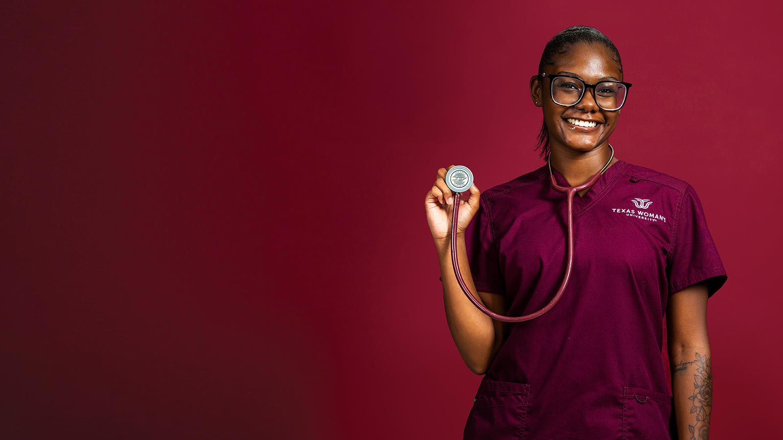 A TWU Nursing student in a set of maroon scrubs with a stethoscope around her neck