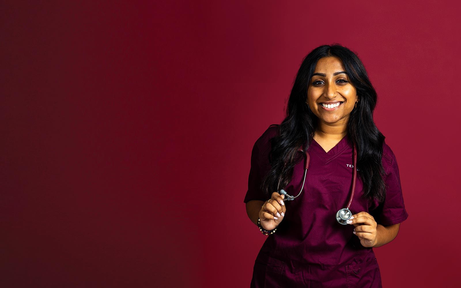 A TWU student wearing maroon scrubs and holding a stethoscope draped around her neck