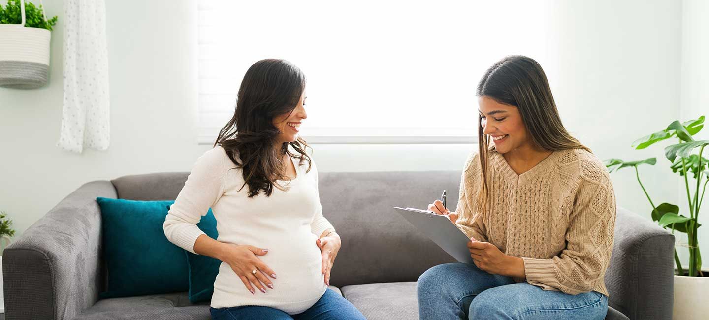 A doula sits in an office setting with a pregnant patient and takes notes.